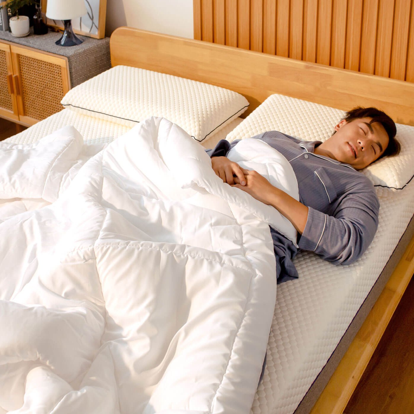 Person lying in bed with white comforter and pillows, wooden headboard and nightstand.