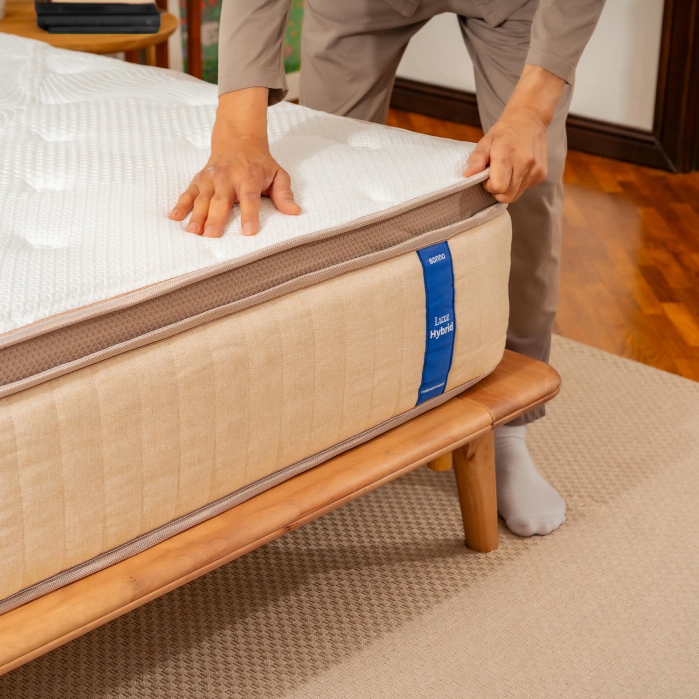 Person adjusting a mattress on a wooden bed frame with a blue tag.