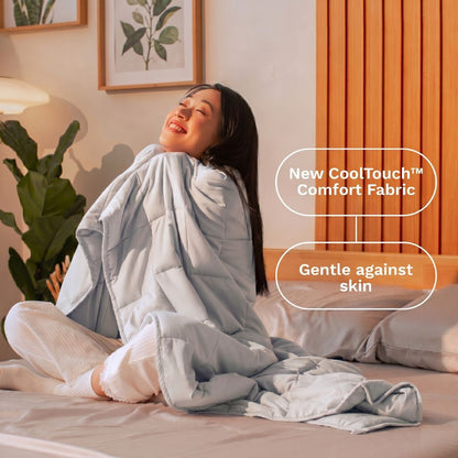 Woman sitting on a bed wrapped in a gray comforter with text about 'New CoolTouch Comfort Fabric' and 'Gentle against skin'.