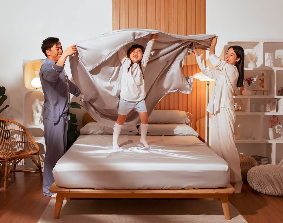 Family of three making a bed together in a cozy bedroom.