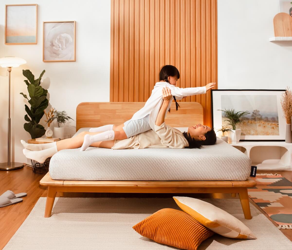 Two people playing on a bed in a cozy bedroom with wooden furniture and decor.