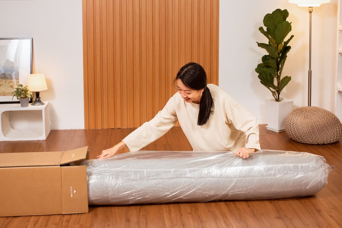 Person unboxing a large item wrapped in plastic on a wooden floor.