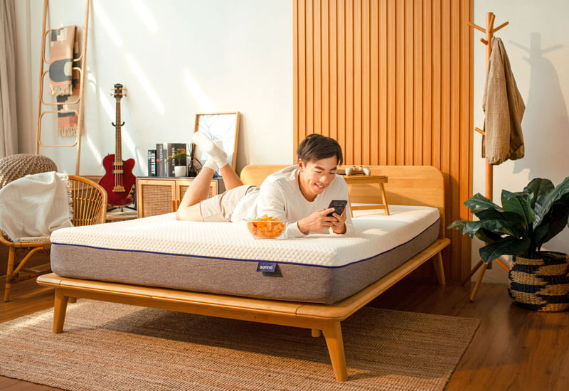 Person lying on a mattress in a bedroom using a smartphone