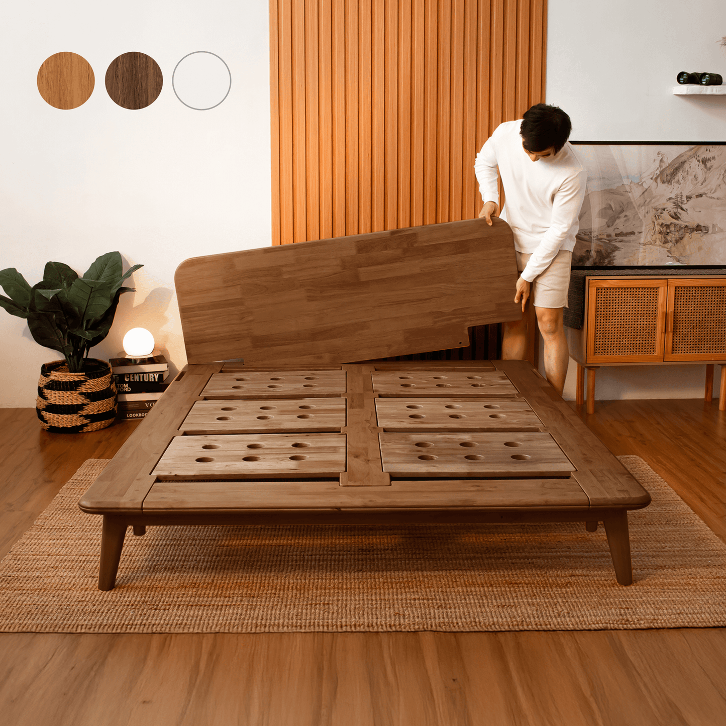 Person assembling a wooden bed frame in a room with a plant and lamp.