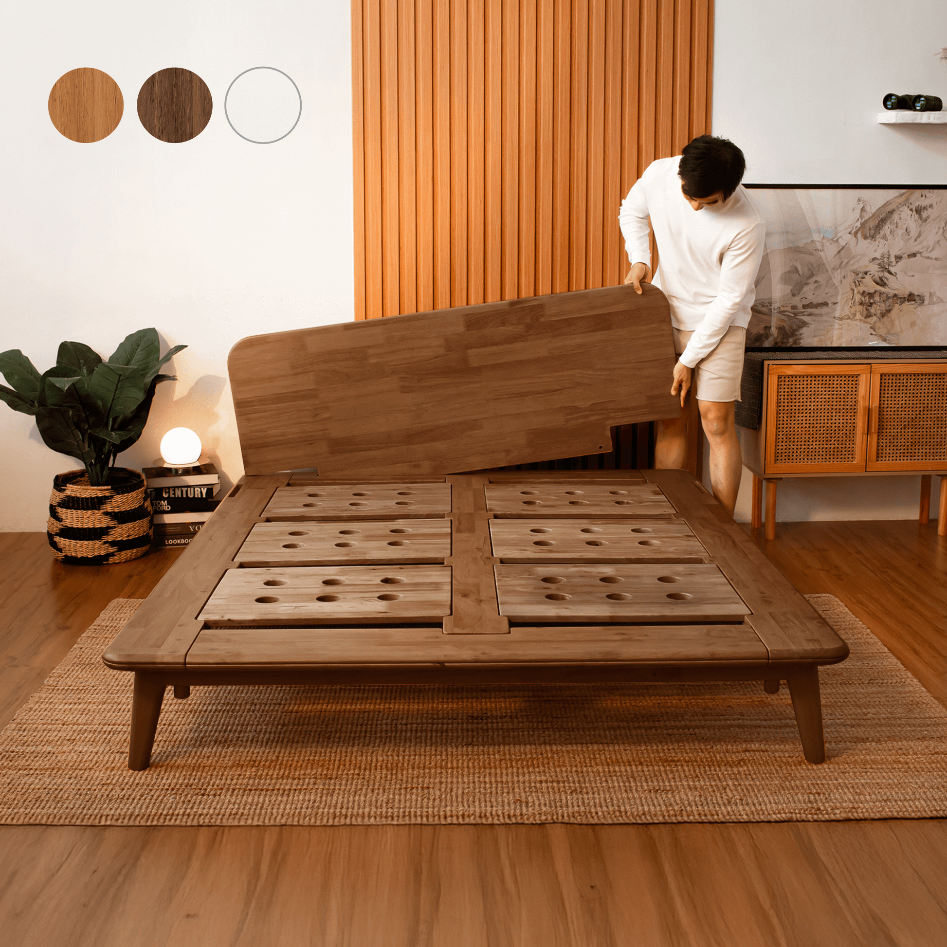 Person assembling a wooden bed frame in a room with a plant and lamp.