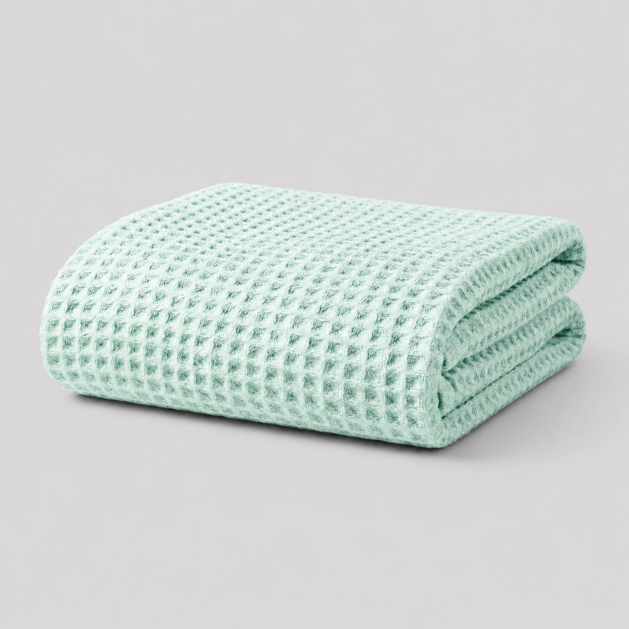 Folded sage green Sonno waffle-textured bamboo blanket on a light grey background