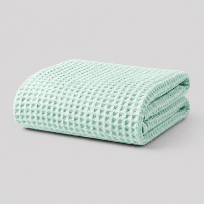 Folded sage green Sonno waffle-textured bamboo blanket on a light grey background