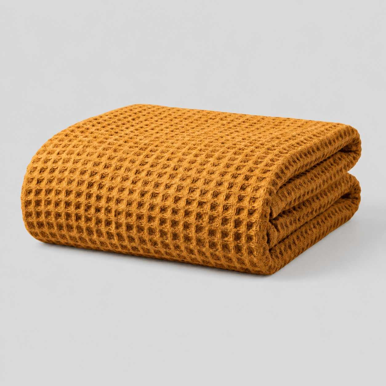 Folded mustard yellow Sonno waffle-textured bamboo blanket on a light grey background