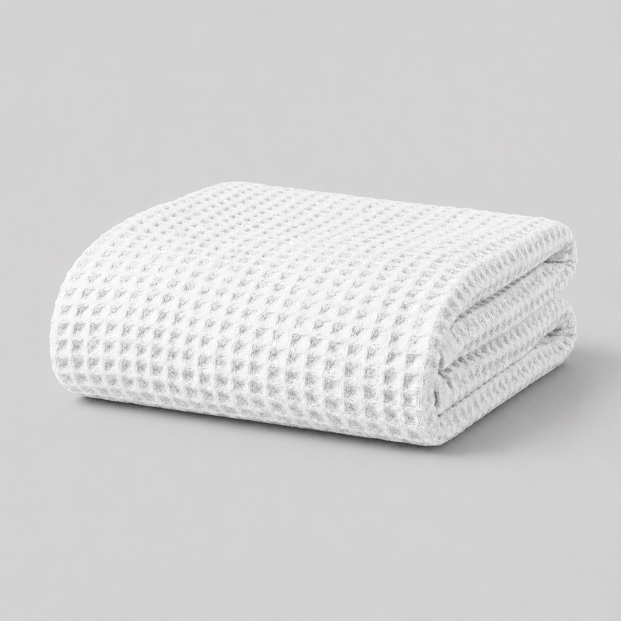 Folded white textured Sonno waffle bamboo blanket on a grey background
