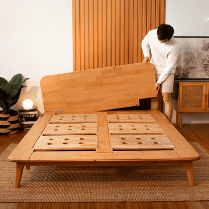 A person assembling a beige Sonno Signature Bed Frame made of wood, in a room with wooden walls and flooring.