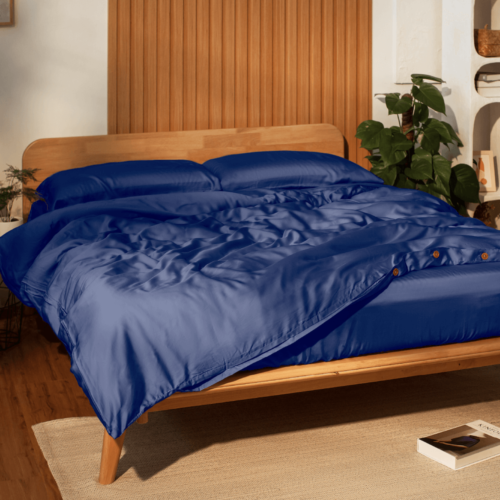 Blue comforter on a wooden bed in a room with plants and shelves.