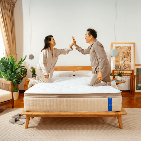 Two people giving each other a high-five over a mattress in a bedroom setting.