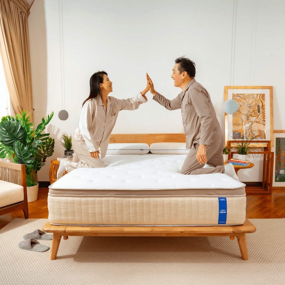 Two people giving each other a high-five over a Sonno Luxe Hybrid mattress in a bedroom setting.