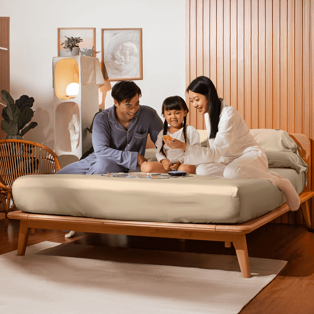 Family of three sitting on a bed in a cozy room.