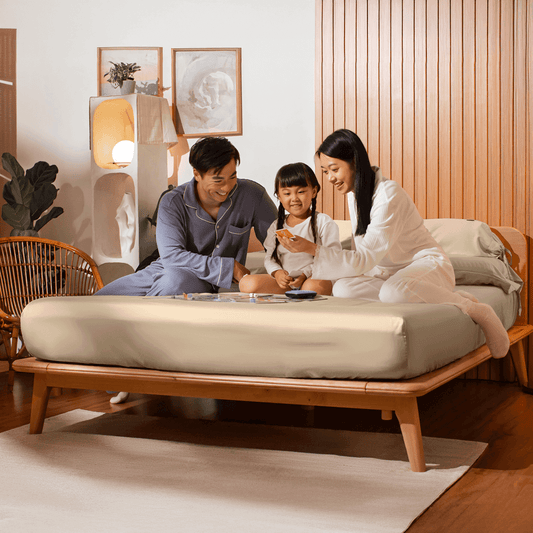 Family of three sitting on a bed in a cozy room.