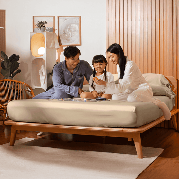 Family of three sitting on a bed in a cozy room.