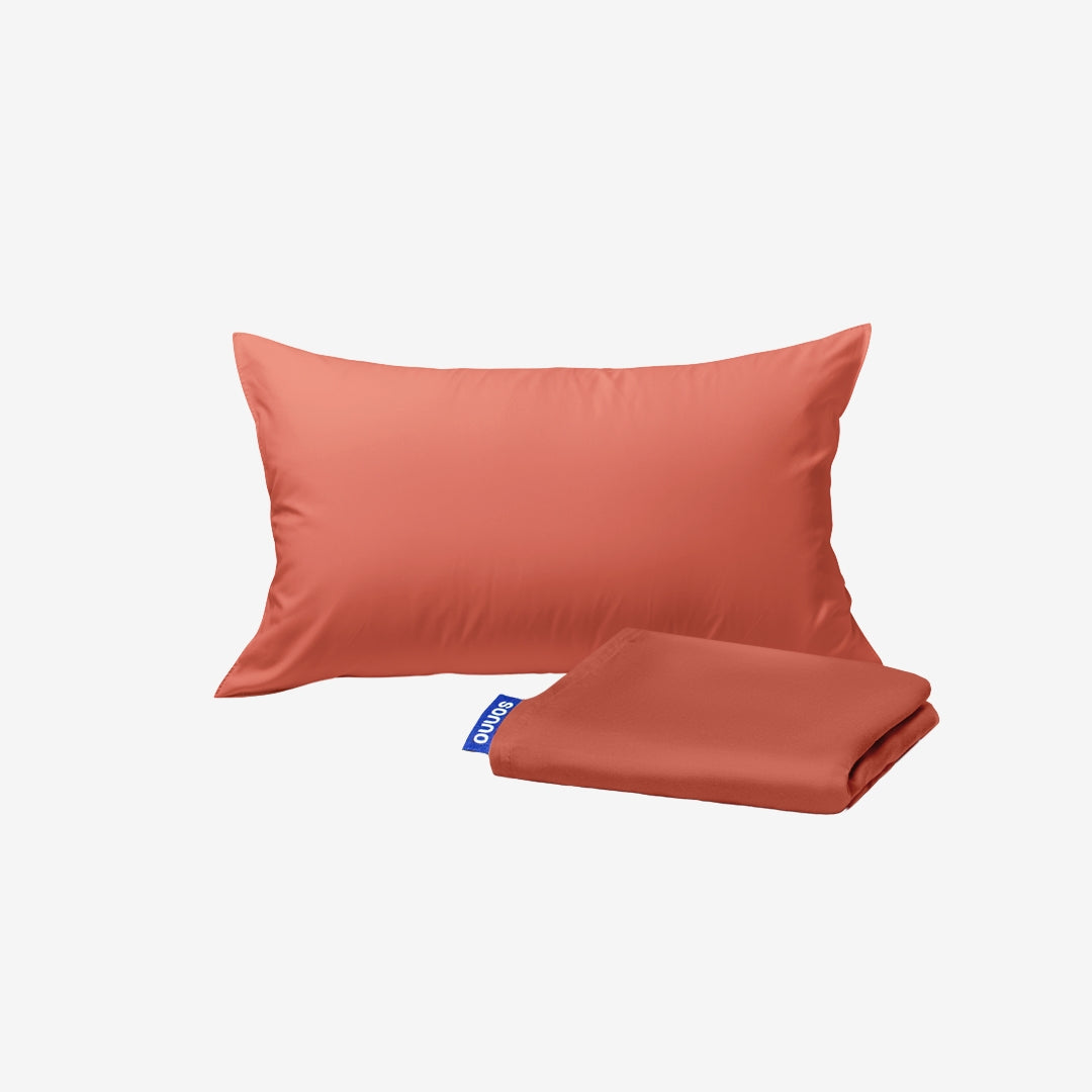Coral-colored pillow and folded blanket on a light gray background